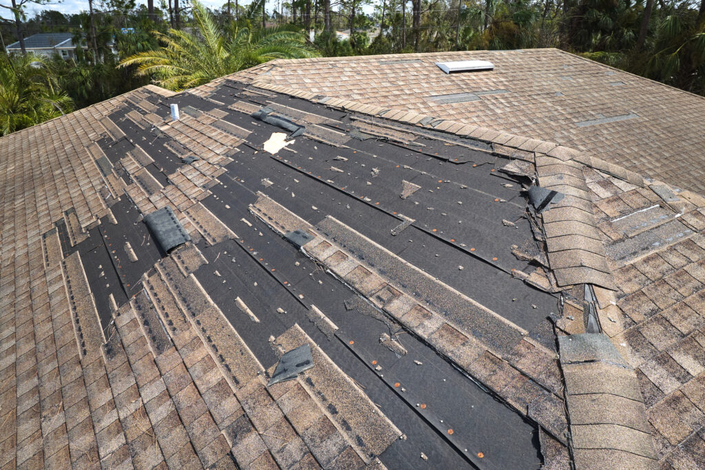 Wind damaged house roof with missing asphalt shingles after hurricane Ian in Florida. Repair of home rooftop concept