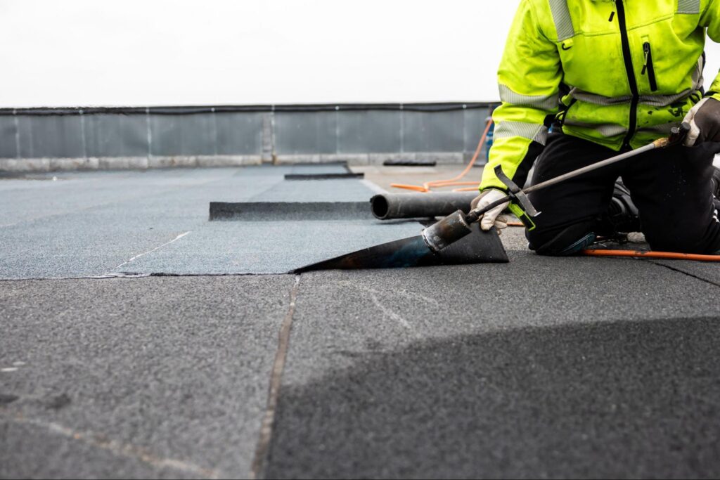 person in bright yellow work outfit working on a roof laying on the roof